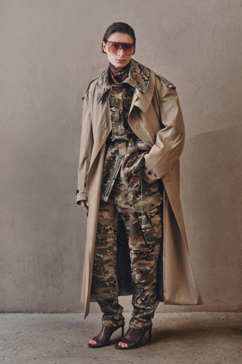 Maskáče v elegantnější společnosti. Značka Co pro Pre-Fall 2026 vrství výrazný camo komplet pod klasický béžový trenčkot a ukazuje, že vojenský vzor může fungovat i v sofistikovaném městském stylingu. Foto: Co, Pre-Fall 2026